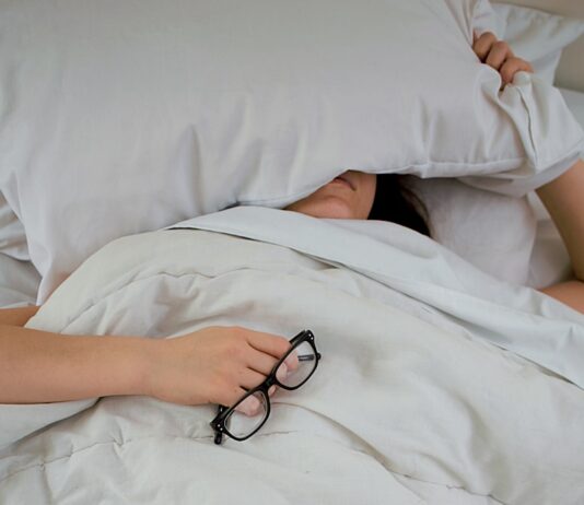 뱃살 타파의 신비, 수면의 역할은 무엇일까? 전문가들의 설명 person lying on bed while covering face with pillow and holding eyeglasses