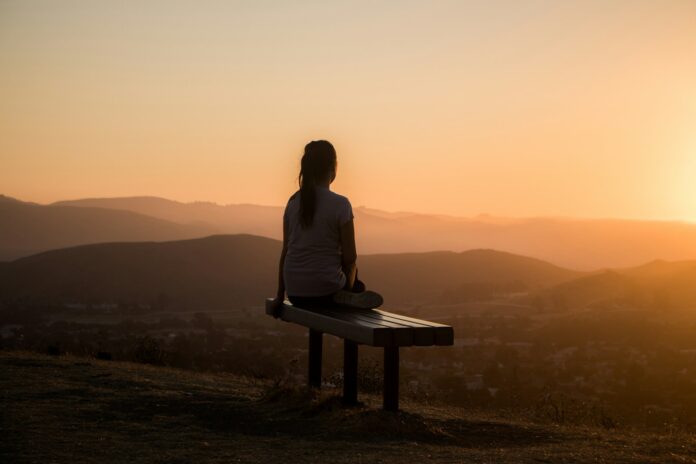 Photo by Sage Friedman woman sitting on bench over viewing mountain