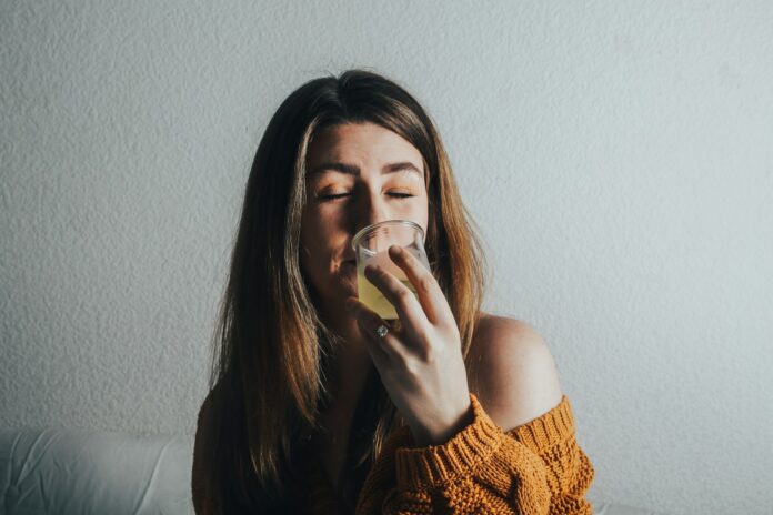 Photo by Giorgio Trovato a woman drinking a glass of water on a couch